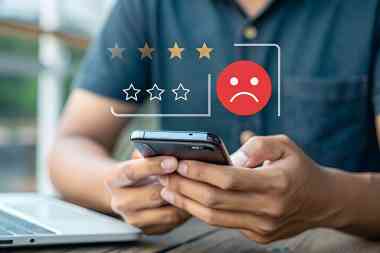 © main_asn - stock.adobe.com Mann bedient Smartphone, darüber negatives Smiley und schlechte Sterne Bewertung